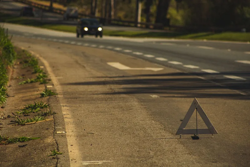Awaria ciężarówki w Niemczech – praktyczne zwroty 1 Trójkąt ostrzegawczy ustawiony na jezdni o zmierzchu, w tle nadjeżdżający samochód z włączonymi światłami