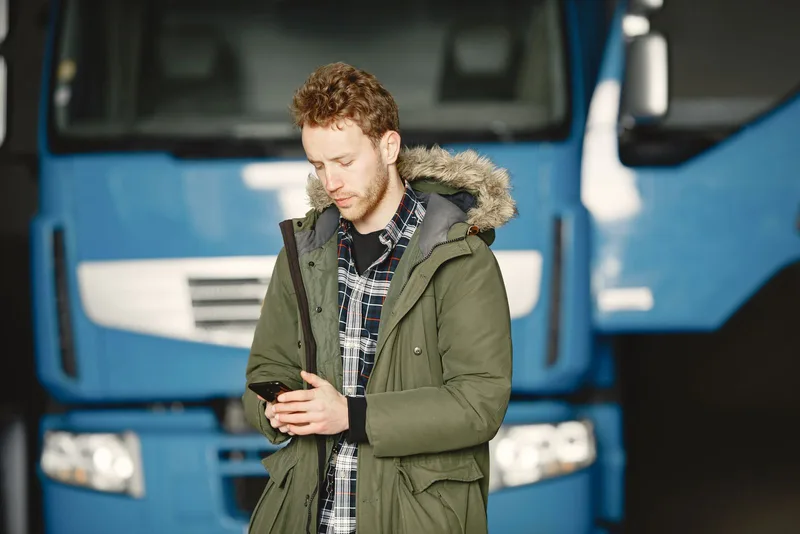 Rozmowa telefoniczna po niemiecku dla kierowcy zawodowego 1 Kierowca ciężarówki rozmawia przez telefon, stojąc przed niebieską kabiną pojazdu
