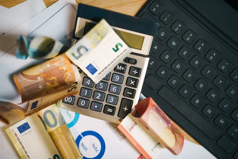 6 klasa podatkowa w Niemczech – dlaczego pracownik do niej trafia? 2 Banknoty euro, kalkulator i klawiatura symbolizujące rozliczanie dochodów z kilku miejsc pracy