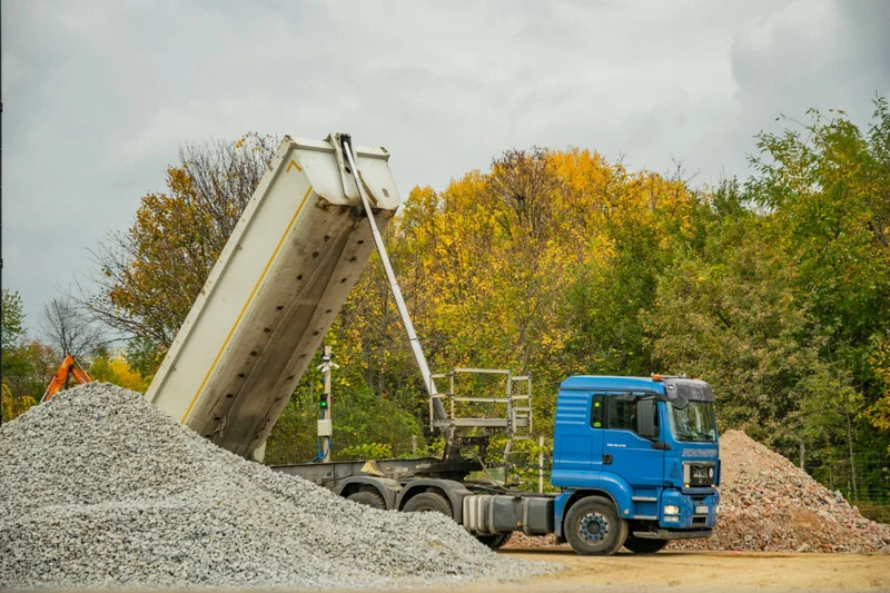 Silos czy wywrotka – porównanie codziennej pracy kierowcy 2 Wywrotka rozładowuje kruszywo na placu budowy, skrzynia ładunkowa uniesiona do góry